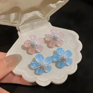 Close-up of pink and blue resin flower stud earrings with zircon centers in a shell box