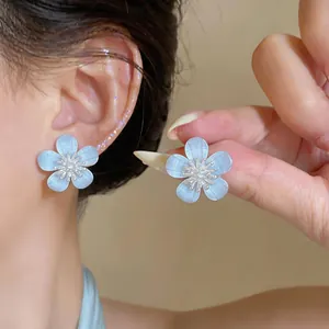 Close-up of light blue resin flower stud earrings with zircon centers shown on ear