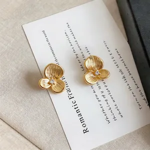 Close-up of golden 3-petal flower stud earrings with a clear crystal on a decorative card