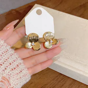 Macro detail of elegant gold-tone camellia flower stud earrings with a sparkling center stone