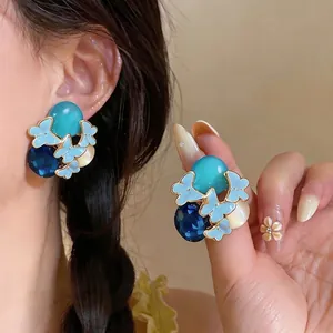 Blue butterfly stud earrings with oval resin stones and crystal accents on a model's ear