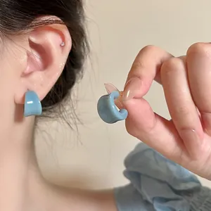 Gros plan de boucles d'oreilles émaillées bleues en U, portées à l'oreille et tenues.