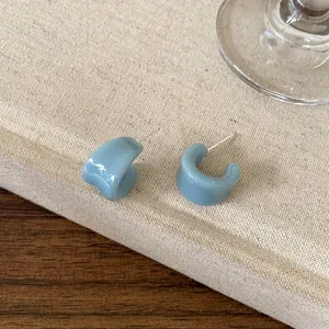 Détail macro de boucles d'oreilles en émail bleu en forme de U sur fond de tissu beige