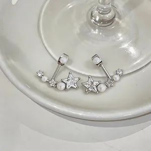 Primo piano di orecchini a stella in argento con zirconi e perle su ceramica bianca