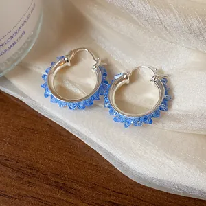 Close-up detail of elegant silver-colored hoop earrings with shining blue glass crystals