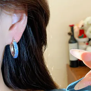Detailed view of elegant silver hoop earrings with blue glass inlay worn on a female ear