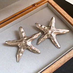 Detailansicht silberner Seestern-Ohrringe aus Metall mit strukturierter Oberfläche.