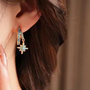 Close-up detail of gold-plated hoop earrings featuring a turquoise star pendant.