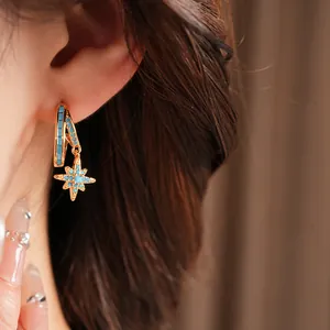 Detail showing a gold star-shaped earring with blue turquoise stones worn on the ear