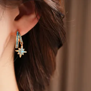 Macro detail of a gold double-layered hoop earring with a turquoise star pendant