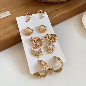 Detailed view of vintage gold metal earring set with hearts and pearls on a white display card