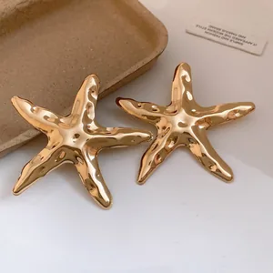 Makroaufnahme goldfarbener, glänzender Seestern-Ohrringe mit strukturierter Oberfläche.
