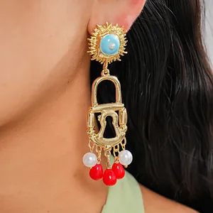 Close-up detail showing a vintage gold padlock earring with pearls and red acrylic tassels.