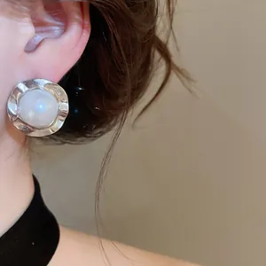 Detailed view of elegant silver textured metal earrings with a pearl center on ear
