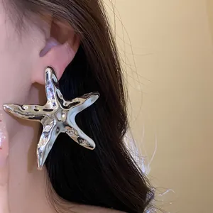 Detailaufnahme eines silbernen Seestern-Ohrrings mit Faltenstruktur am Model.