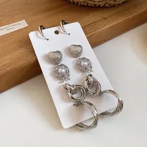 Detail view of silver-toned metal earring set with heart studs and hoop designs