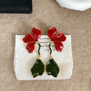 Detailed view of long red enamel flower drop earrings featuring green stems and leaf