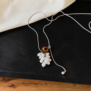 Detail view of a silver-toned necklace featuring a tiger eye and pearl grape pendant.