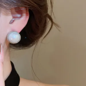 Close-up of elegant round pearl stud earring with silver textured border on model's ear.