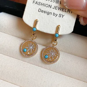 Détail macro de boucles d'oreilles soleil en plaqué or 18 carats avec turquoises