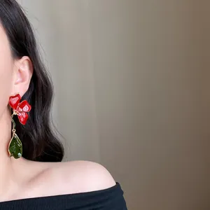 Close-up detail view of elegant long red flower drop earring with green leaf pendant on model