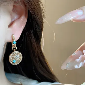 Gros plan d'une boucle d'oreille créole plaquée or 18 carats avec zircons et turquoise.