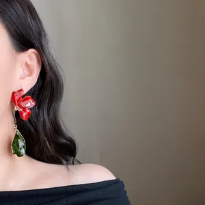 Detail view of large red enamel flower earrings with green leaf dangle on a model