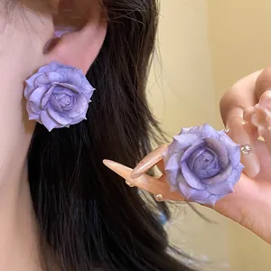 Close-up of elegant purple resin rose stud earrings on ear and held by hand