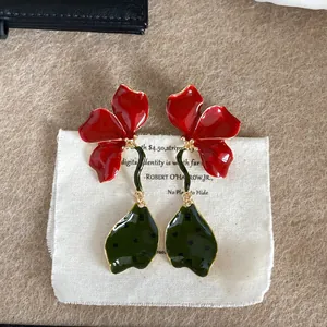Macro shot of oversized red enamel flower earrings with dark green dotted leaves