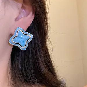 Close-up of a vintage-style blue enamel flower stud earring with gold-toned border