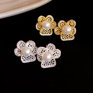 Primer plano de elegantes pendientes de flores huecas en oro y plata con perlas