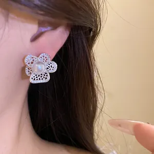 Detalle de un elegante pendiente de flor hueca con perla central lucido en la oreja.