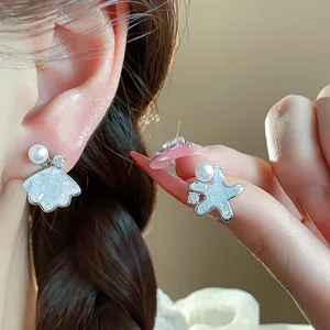 Close-up of asymmetric shell and star stud earrings with pearls and zircon stones.