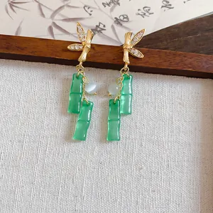 Detailed view of elegant gold bamboo leaf earrings with green resin bamboo joint tassels.