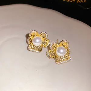 Primer plano detallado de pendientes de flores doradas huecas con perlas y circonitas