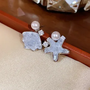 Detailed view of asymmetric star and shell stud earrings with elegant pearls and crystals.