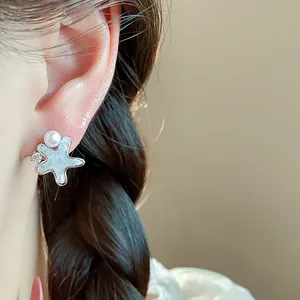 Close-up of delicate starfish earring with pearl and zircon detail on model's ear