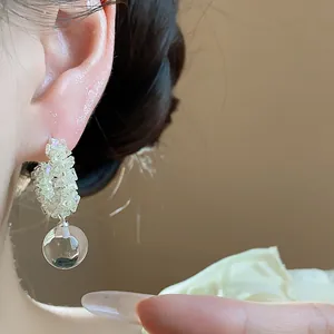 Close-up of silver needle earrings with shimmering beads and a clear glass ball drop.