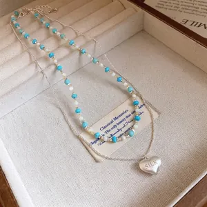 Minimalist double layer necklace with blue beads and silver heart pendant in jewelry box.