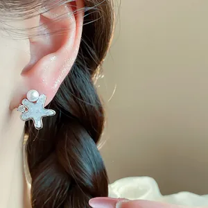 Close-up of a silver-toned star earring featuring shell inlay, a pearl, and zircon detail.