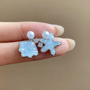 Detailed view of asymmetric shell and star stud earrings with white pearls and zircons