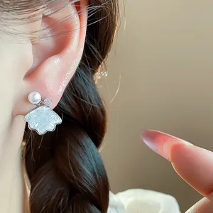 Detailed close-up of a silver fan-shaped earring with pearl and zircon on a model's ear