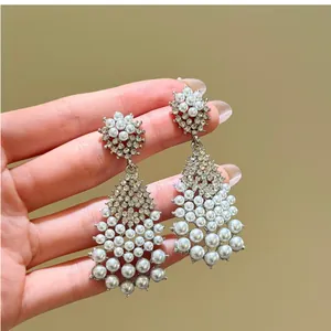 Close-up of elegant silver chandelier earrings with pearls and zircons held by hand