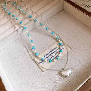 Detail view of a layered silver necklace with a frosted heart pendant and turquoise beads
