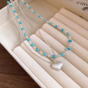 Detailed view of double-layer necklace with blue beads and brushed heart pendant