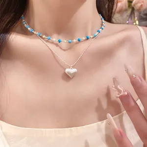 Close-up shot of a double-layered necklace featuring a white heart pendant and blue beads