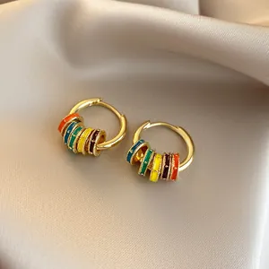 Close-up of colorful enamel hoop earrings with gold-plated finish on silk background.