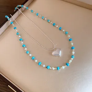 Close-up of a minimalist layered necklace with heart pendant and blue beads in a gift box