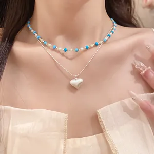 Detail of a layered necklace featuring a blue beaded choker and silver heart pendant