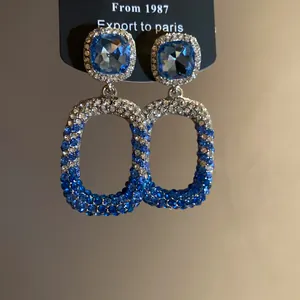 Elegante primo piano di orecchini pendenti quadrati con cristalli blu e bianchi lucenti